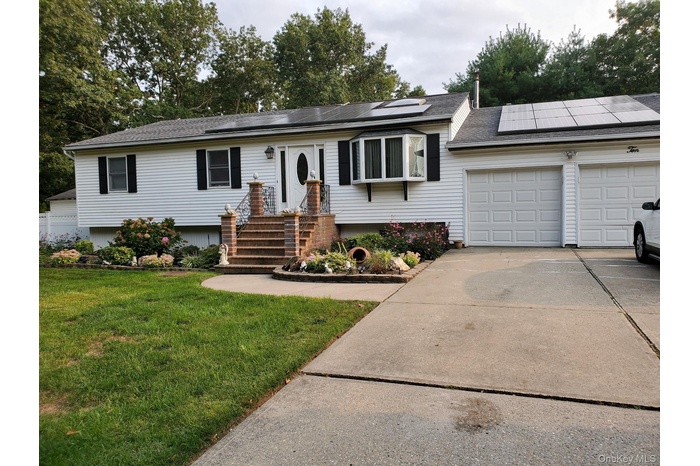 Single story home with a front lawn, driveway, a shingled roof, roof mounted solar panels, and an attached garage