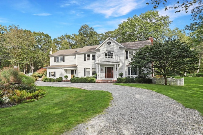 View of front of house with a front lawn, driveway, a chimney, and view of wooded area