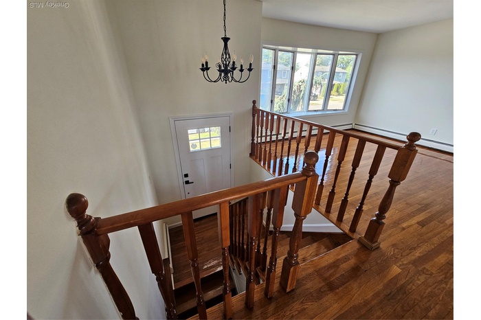 Stairway featuring wood finished floors, a chandelier, and a baseboard heating unit