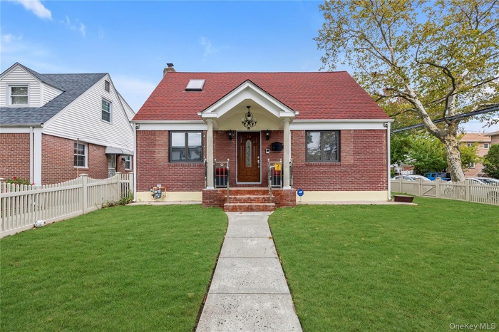 View of front facade featuring brick siding, a shingled roof, a chimney, and covered porch