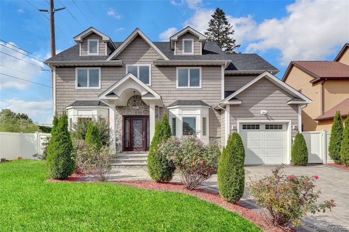 View of front of house with a shingled roof, driveway, an attached garage, and stone siding