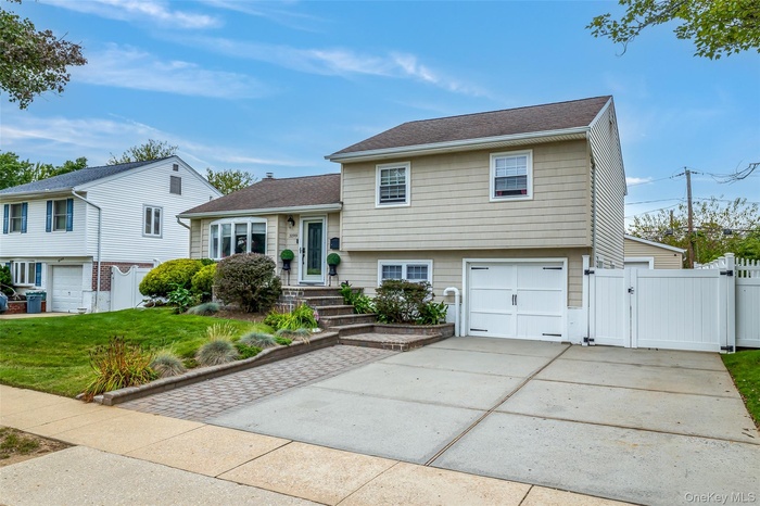 Split level home featuring a gate, a garage, driveway, and a shingled roof
