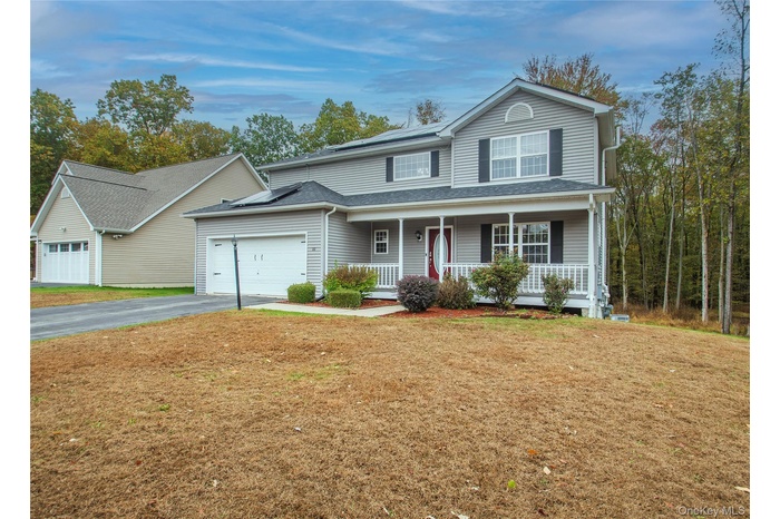 Traditional home with a porch, a front yard, asphalt driveway, roof mounted solar panels, and a garage