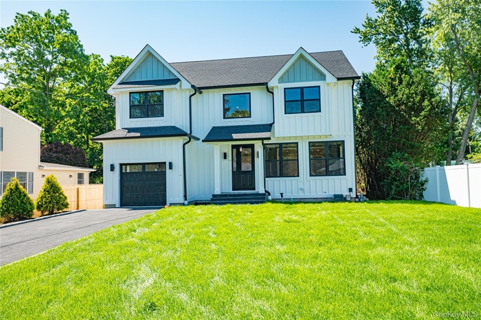 Modern farmhouse featuring a garage, driveway, board and batten siding, and roof with shingles