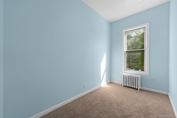 Carpeted empty room with radiator and baseboards