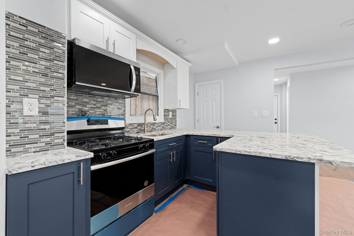 Kitchen featuring stainless steel appliances, a peninsula, blue cabinetry, tasteful backsplash, and white cabinets