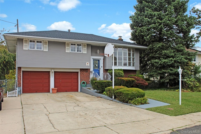 Raised ranch with brick siding, driveway, a chimney, and a garage
