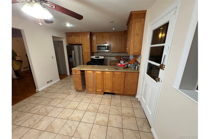 Kitchen featuring brown cabinetry, ceiling fan, appliances with stainless steel finishes, backsplash, and light tile patterned floors