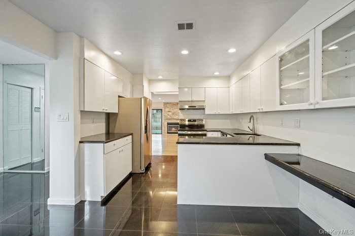 Kitchen with glass insert cabinets, appliances with stainless steel finishes, recessed lighting, white cabinetry, and a peninsula