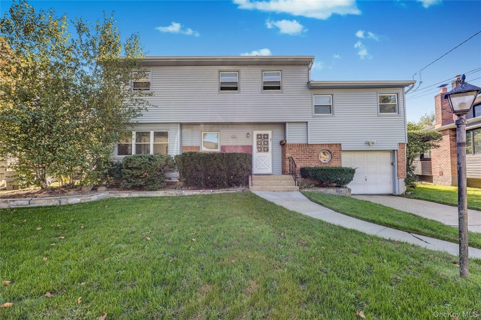 View of front facade with brick siding, a front yard, driveway, and an attached garage