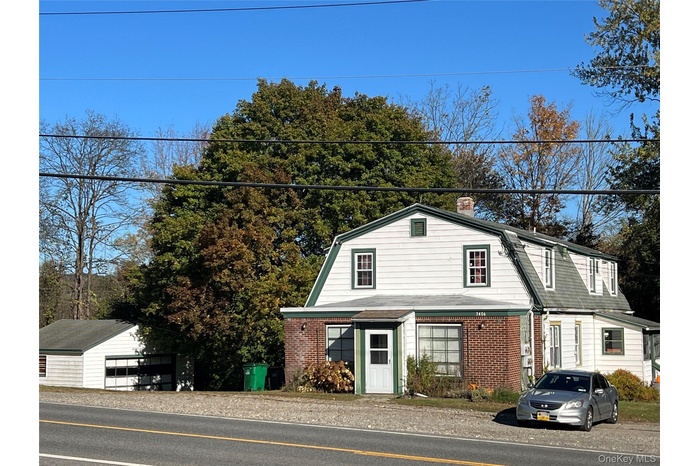 Dutch colonial featuring a gambrel roof, an outdoor structure, brick siding, and a chimney