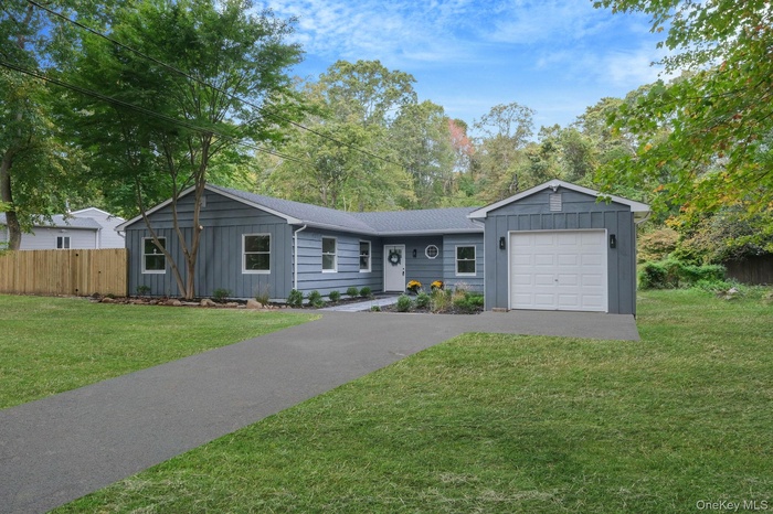 Ranch-style house featuring board and batten siding, a garage, asphalt driveway, and view of wooded area