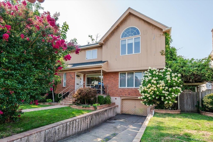 View of front of property featuring a front lawn, an attached garage, covered porch, brick siding, and concrete driveway
