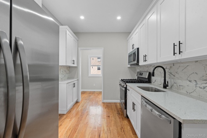 Kitchen featuring appliances with stainless steel finishes, light stone countertops, tasteful backsplash, white cabinets, and recessed lighting