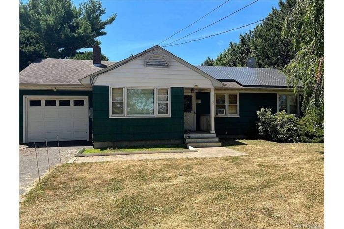 Ranch-style home featuring a front lawn, roof mounted solar panels, a chimney, and an attached garage