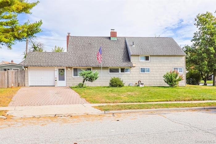 View of front of property featuring a shingled roof, a chimney, decorative driveway, and an attached garage
