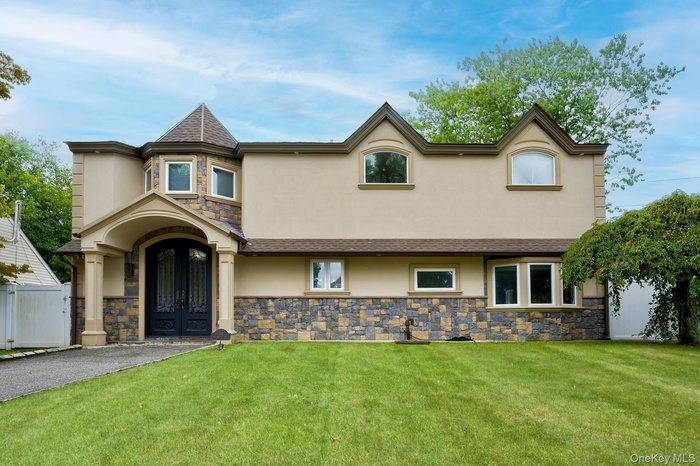 View of front of property with stone siding, stucco siding, a front yard, and roof with shingles