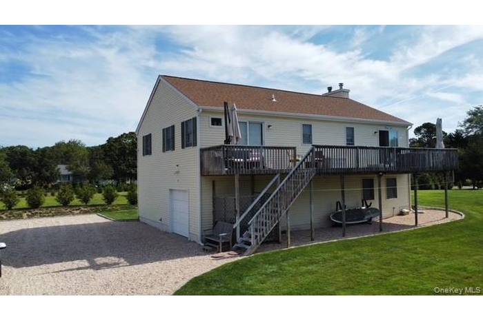 Front view of property featuring a patio, a wooden deck, a lawn, driveway