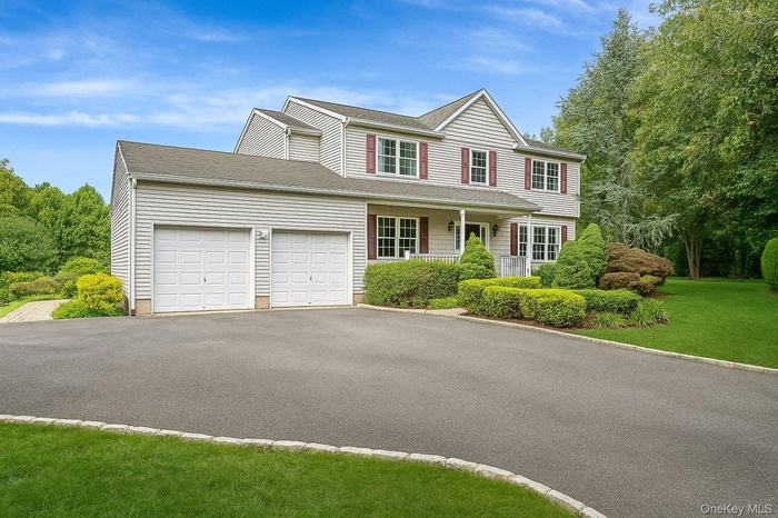 View of front of property featuring driveway, a garage, a porch, a shingled roof, and a front yard