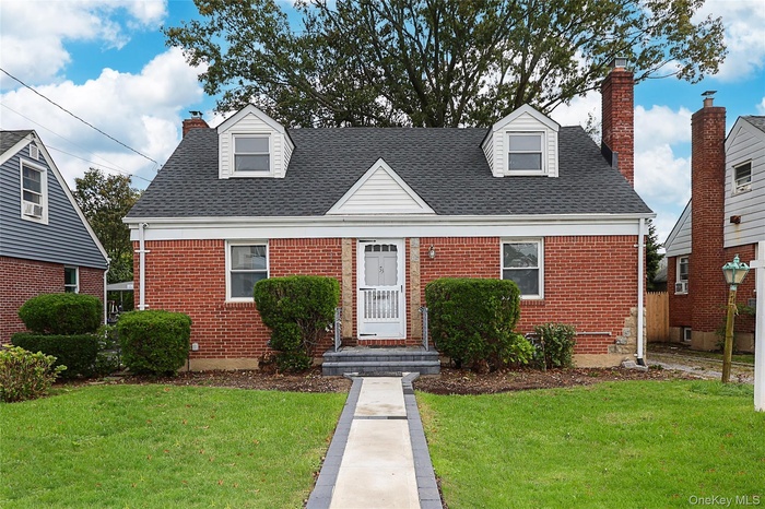 New england style home featuring a front lawn, a chimney, and brick siding