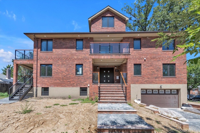 View of front of property featuring a balcony, stairs, brick siding, and a garage
