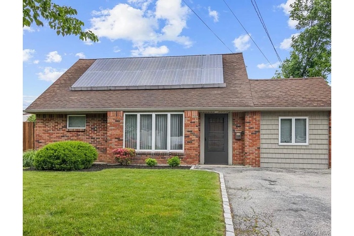 View of front facade featuring a front yard, a shingled roof, roof mounted solar panels, and brick siding