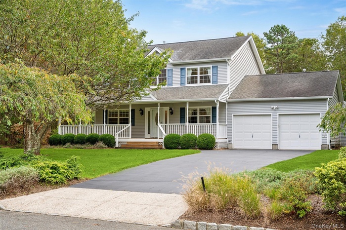 Traditional home featuring roof with shingles, a porch, driveway, a front yard, and a garage