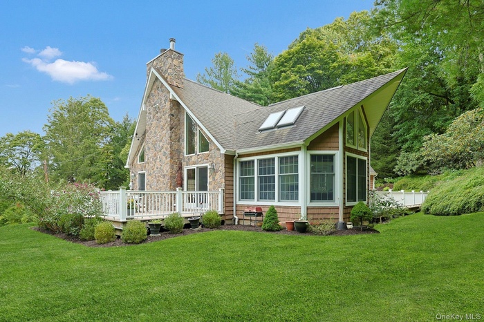 Rear view of house featuring a sunroom, a lawn, roof with shingles, and a chimney