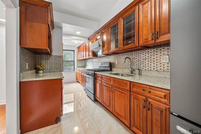 Kitchen featuring light stone counters, stainless steel appliances, decorative backsplash, glass insert cabinets, and recessed lighting