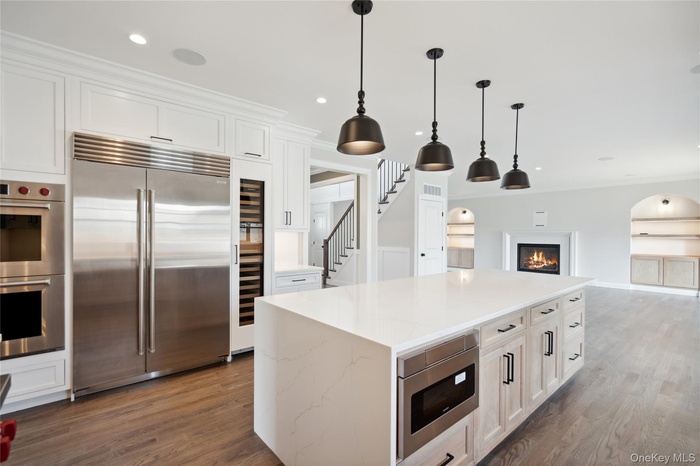 Kitchen featuring built in appliances, wood finished floors, white cabinets, pendant lighting, and open floor plan