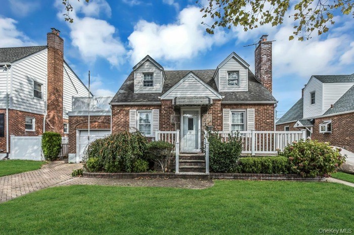 Cape cod home with a front yard, brick siding, an attached garage, and a chimney