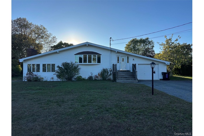 Single story home featuring a front lawn, driveway, a chimney, and an attached garage