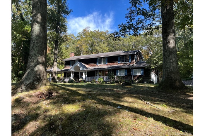 View of front facade with a chimney, covered porch, and a front yard