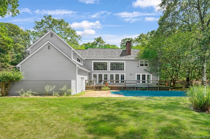 Rear view of house with a wooden deck, a lawn, and a chimney