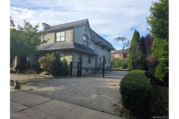 View of front of home with decorative driveway, a gate, stucco siding, and roof with shingles