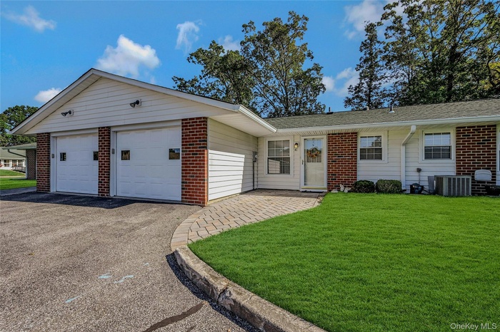Ranch-style home featuring a front lawn, brick siding, asphalt driveway, a patio, and a garage