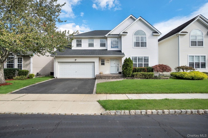 Traditional-style house featuring asphalt driveway, a garage, a front lawn, and a shingled roof