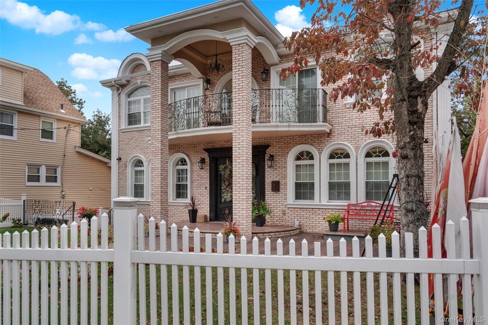 View of front facade featuring brick siding, a balcony, and a fenced front yard