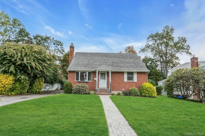 View of front of home with a front yard, a shingled roof, brick siding, and a chimney