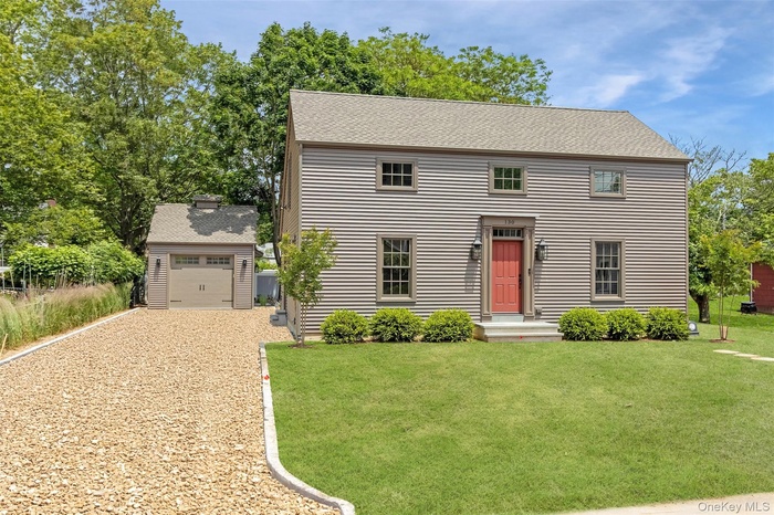 Colonial inspired home featuring gravel driveway, an outbuilding, a front yard, and roof with shingles