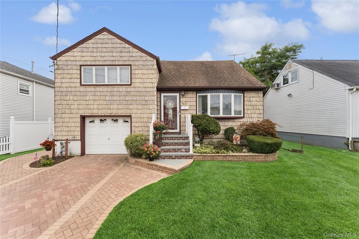Split level home featuring a shingled roof, decorative driveway, and an attached garage