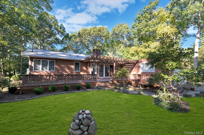 View of front facade featuring a chimney, a front lawn, a deck, and view of scattered trees