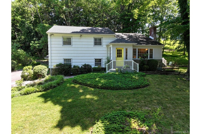 Tri-level home featuring a front yard, a chimney, and view of wooded area