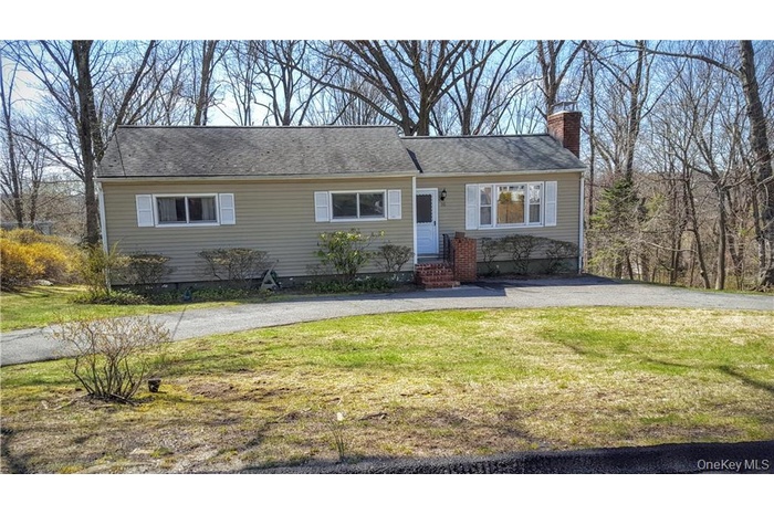 View of front of home with a front yard, a chimney, and driveway