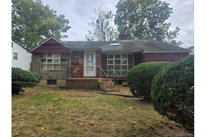 Rear view of house featuring a yard, a chimney, and stone siding