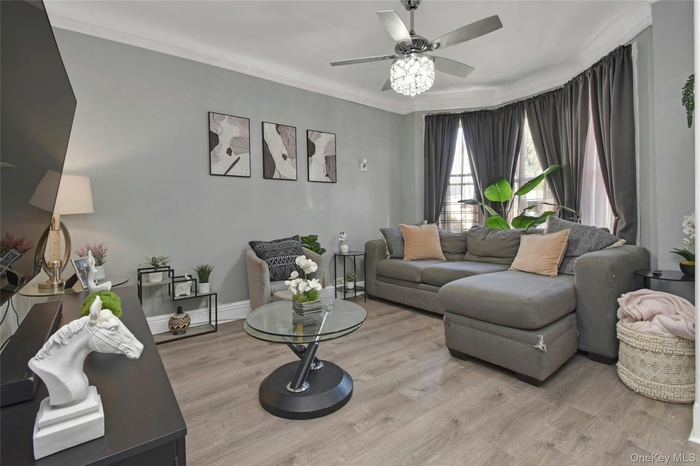 Living area with wood-finished floors, ceiling fan, and crown moldings.