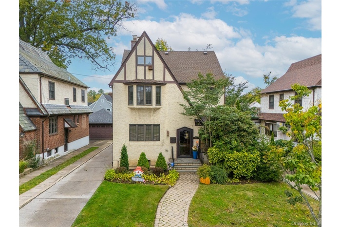 Tudor house featuring a chimney, stucco siding, a front yard, and roof with shingles