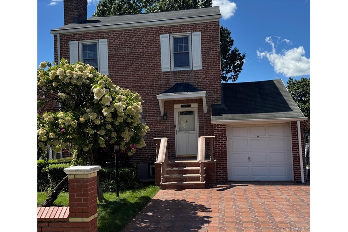 View of front of home featuring a chimney, brick siding, a garage, decorative driveway, and a shingled roof
