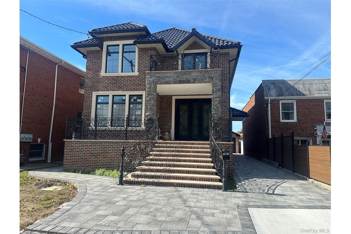 View of front of house featuring a tile roof, brick siding, stone siding, a balcony, and a patio
