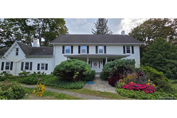 Colonial-style house featuring a chimney, a porch, and a shingled roof